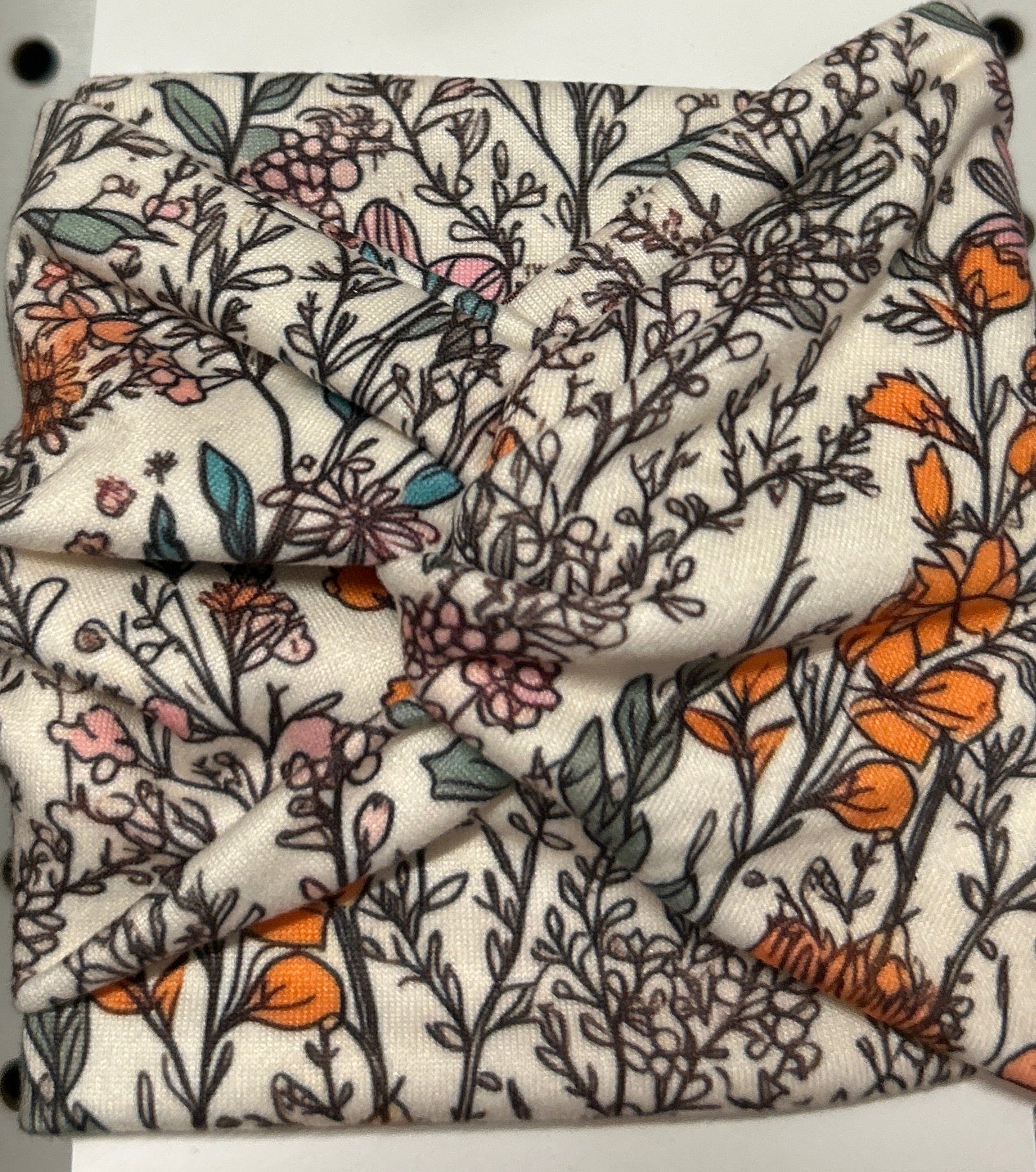 A floral patterned headband, predominantly cream in color with a vintage floral design.